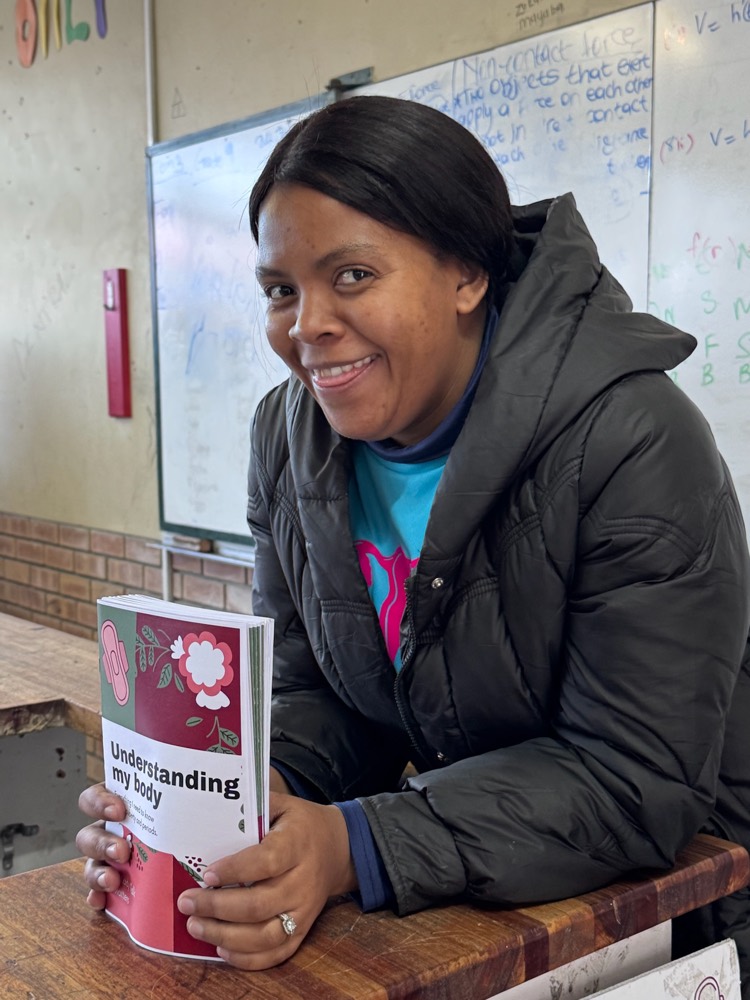 A Lady Talk Matters educator in a classroom holding the 'Understanding my body' booklet